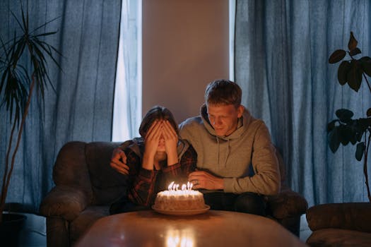 Two friends sharing a heartfelt birthday moment with a cake and candles indoors.