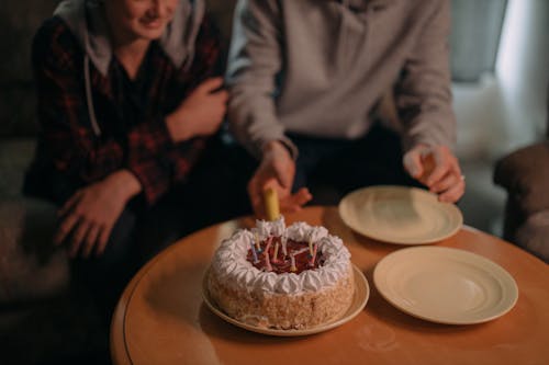 People Sitting at a Table  with a Birthday Cake and Plates