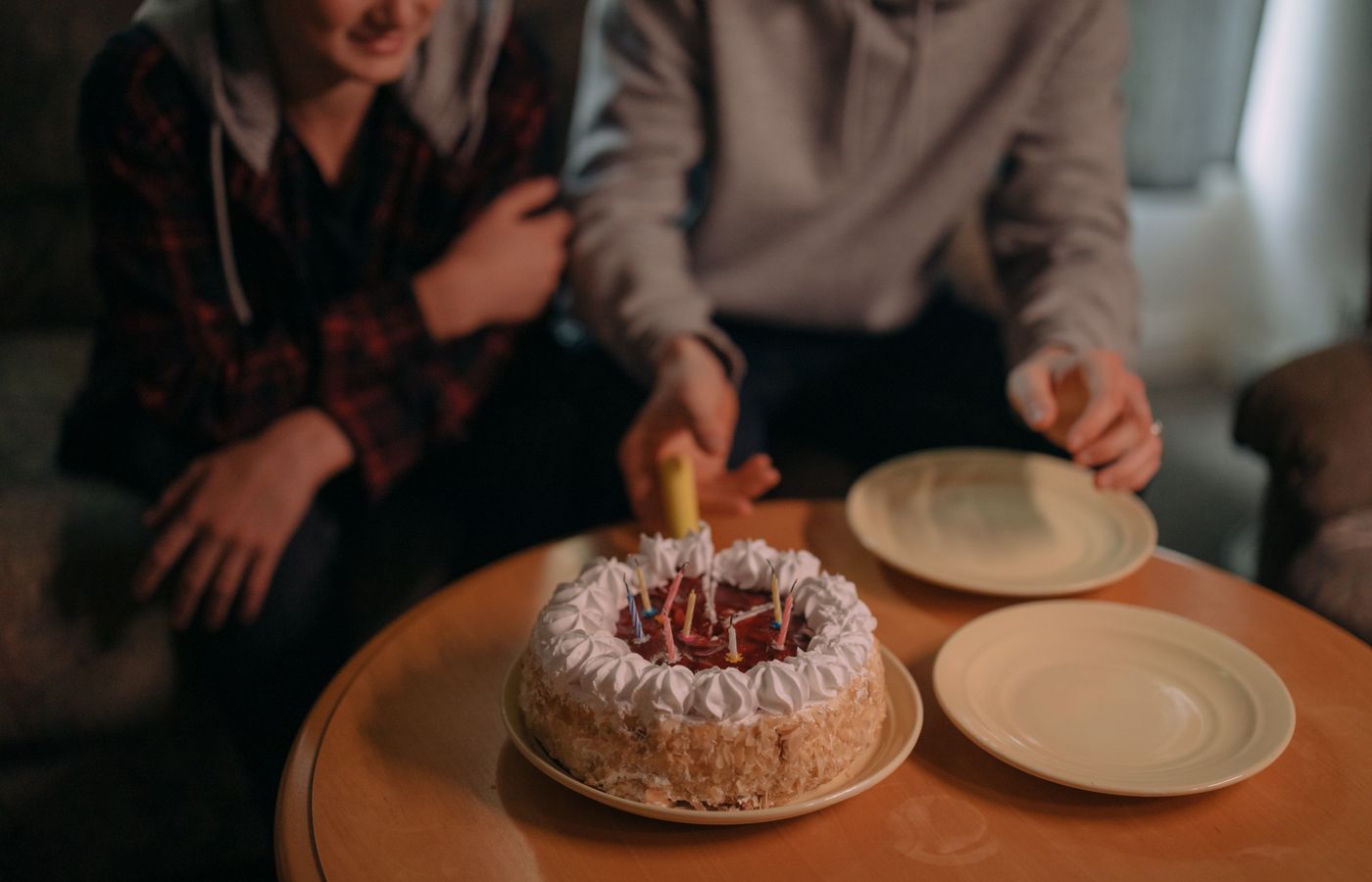Close-up of a birthday cake with lit candles and two friends celebrating indoors.