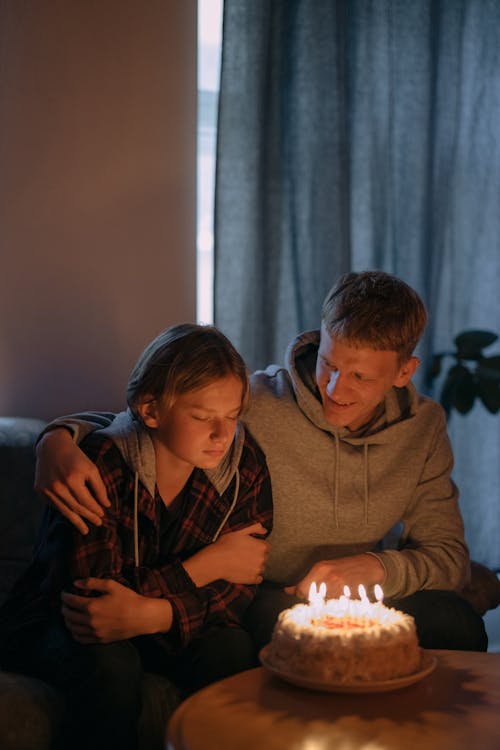 Free A Man Hugging a Young Person Making a Wish on a Birthday Cake Stock Photo