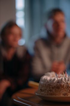 Birthday cake with candles in focus. Two blurred figures in the background, creating depth of field effect.