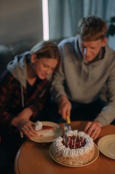 A young couple cutting a birthday cake together in a cozy indoor setting.
