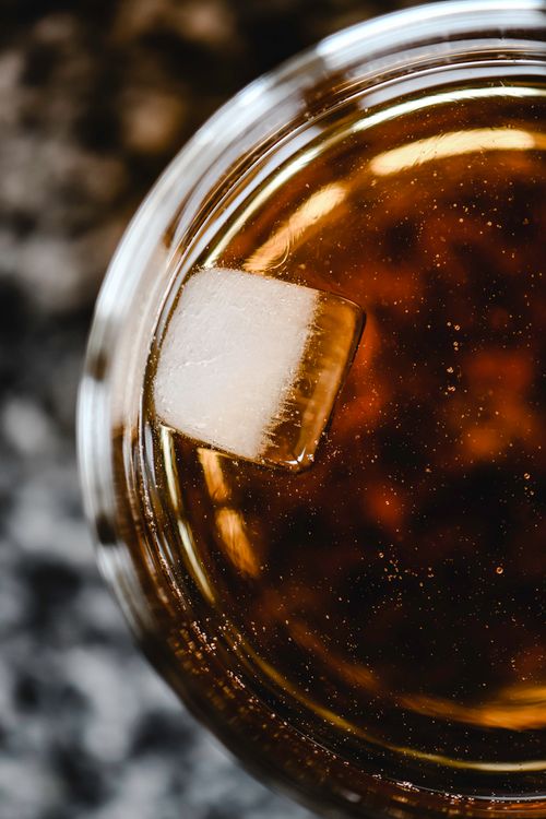 Free Top view of a whiskey glass with a single ice cube, creating a warm, inviting scene. Stock Photo
