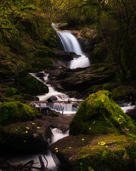 Beautiful cascading waterfall amidst mossy rocks and lush greenery in a tranquil Portuguese forest