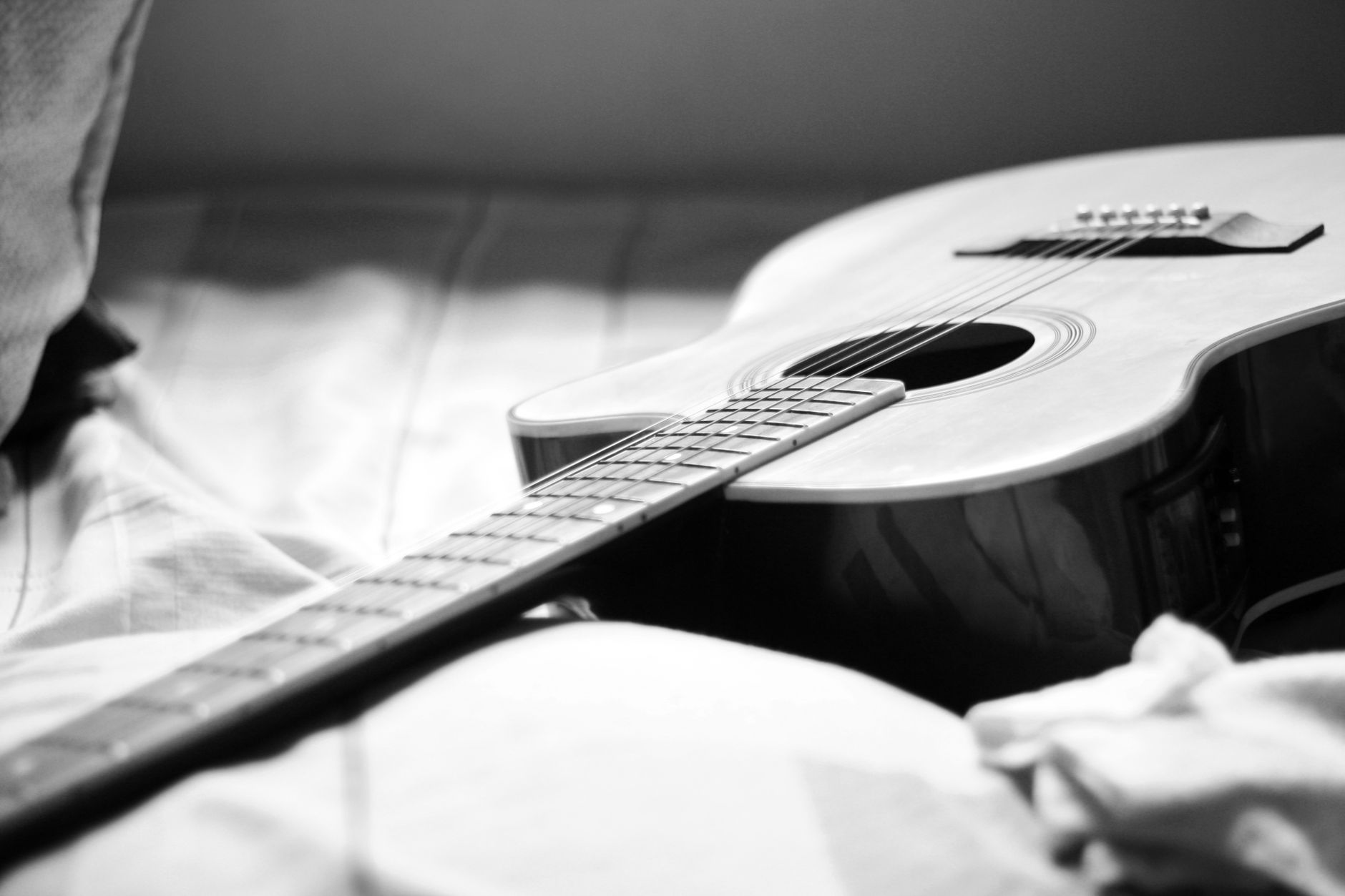 Close-up of an acoustic guitar resting on a bed in a black and white photograph.