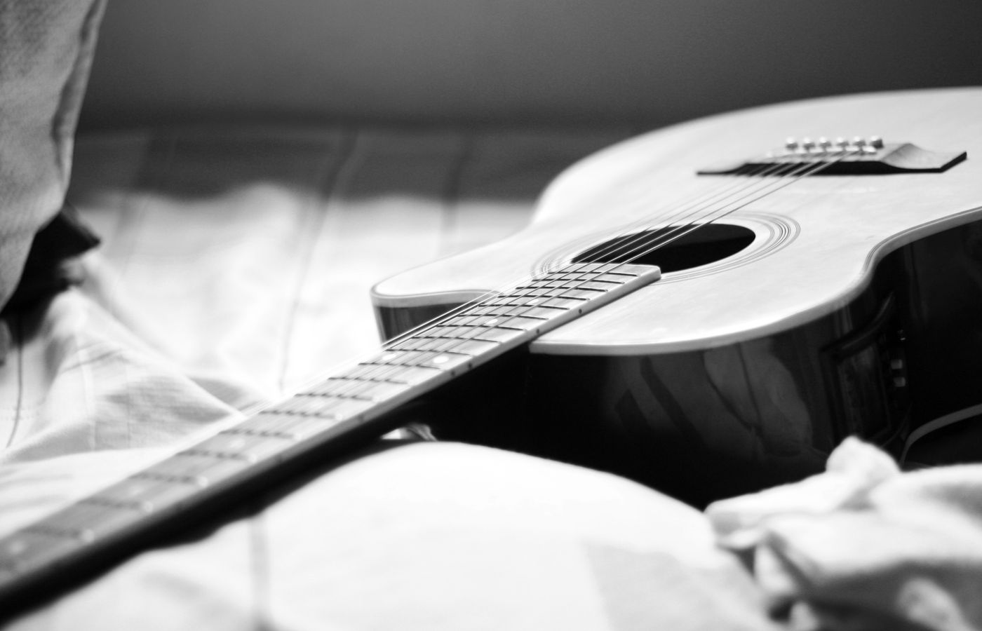 Close-up of an acoustic guitar resting on a bed in a black and white photograph.