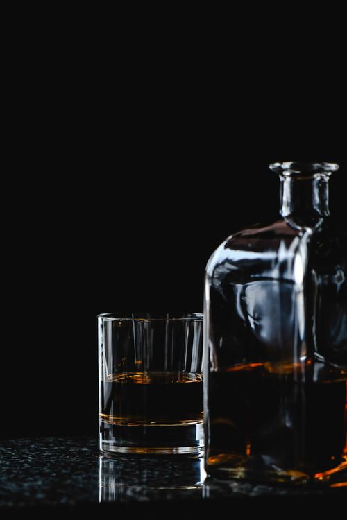 Free A minimalist composition of a glass and bottle of whiskey on a reflective surface against a dark background. Stock Photo