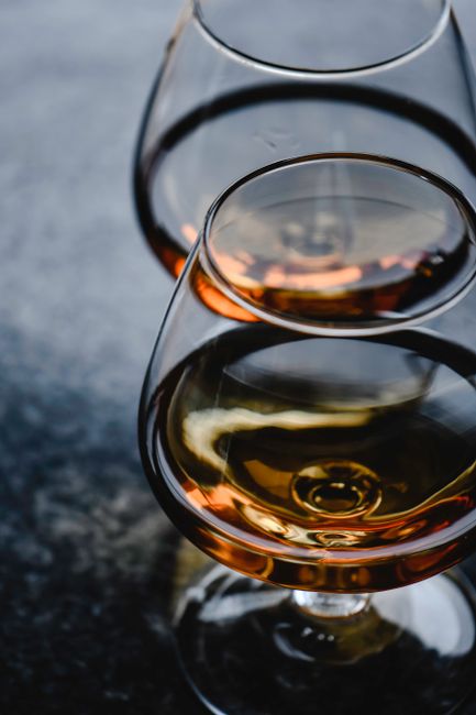 A glass of amber brandy next to an oak aging barrel and a bunch of wine grapes.
