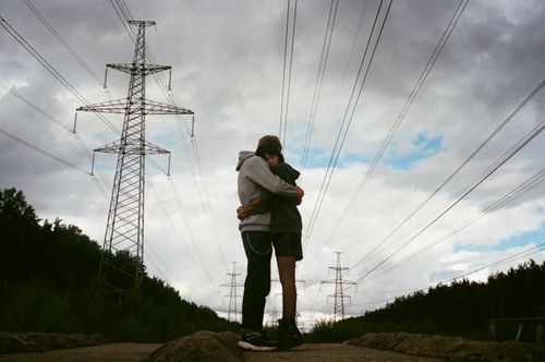 Free Couple hugging beneath power lines under a cloudy sky, showcasing a moment of affection and connection. Stock Photo