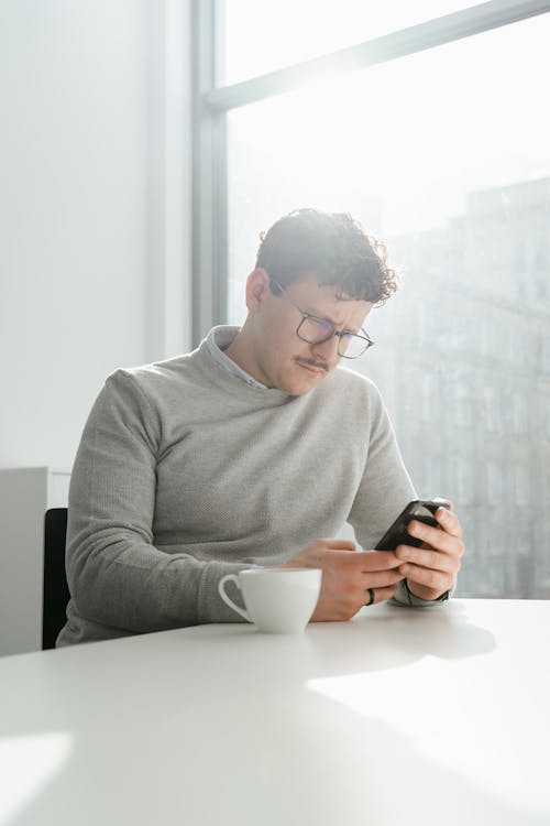 Man in Gray Sweater Using Black Smartphone