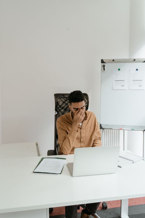 Free A businessman in brown long sleeves feeling stressed while sitting at an office desk. Stock Photo