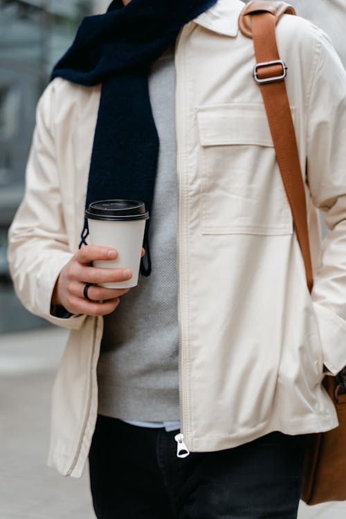 Person in Cream Jacket Holding a Disposable Cup