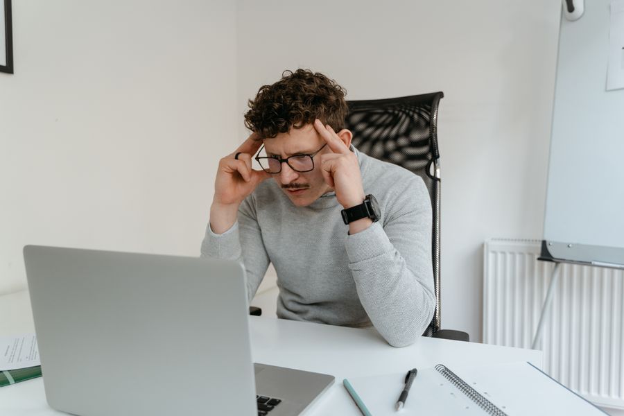 Curly-haired man concentrates while working on a laptop in a modern office setting.