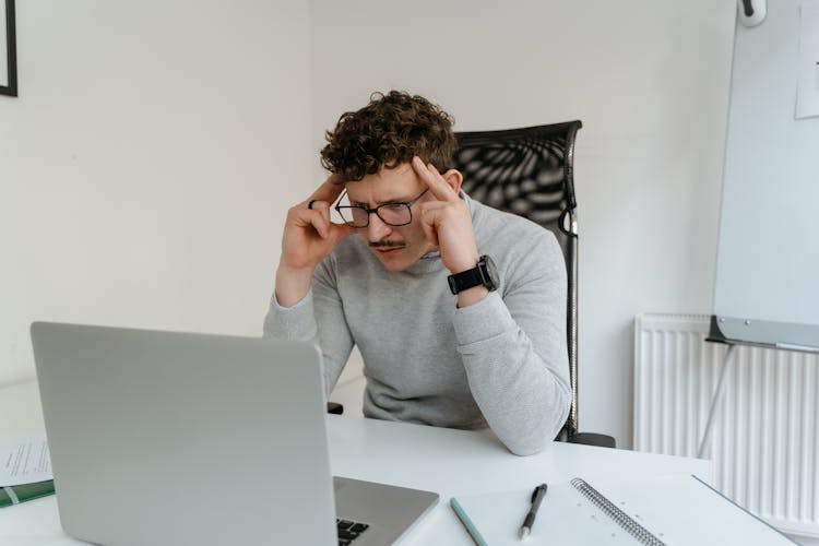 A Man In Gray Sweater Looking At His Laptop With His Hands On His Head