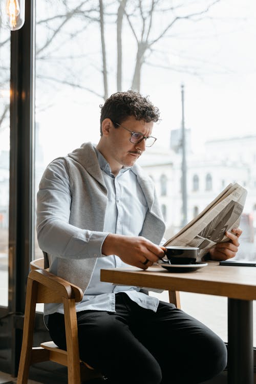 Free Man Holding a Cup While Reading Newspaper Stock Photo