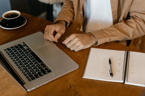 Free Close-up of a man working with a laptop and notebook on a wooden desk. Stock Photo