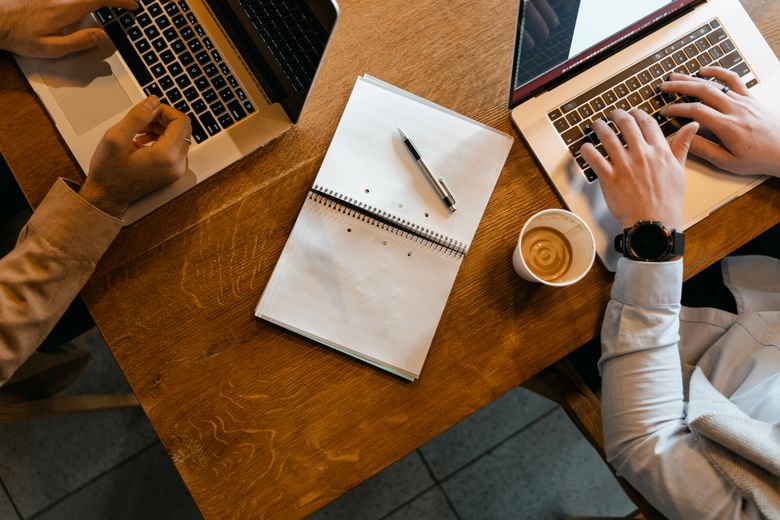 Two people working at laptops across a wooden table — photo by MART PRODUCTION on Pexels