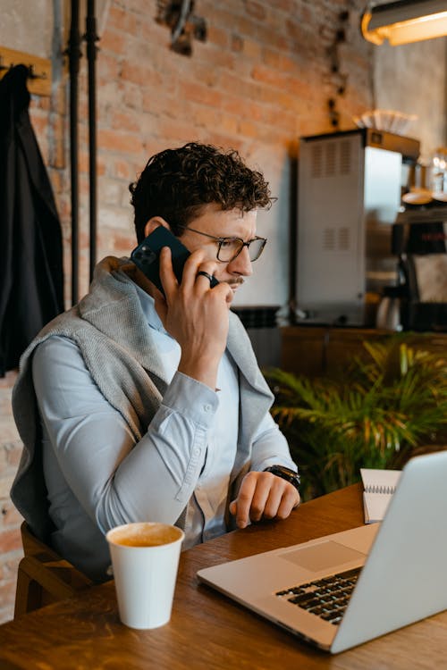 Free A Man in White Long Sleeves Sitting Near the Table while Talking on the Phone Stock Photo