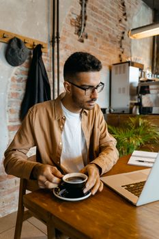 A focused man enjoying a coffee while working on his laptop in a stylish cafe.