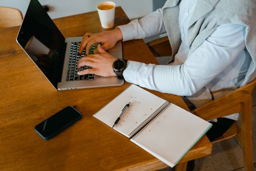 Free Person using laptop with notebook and coffee on a wooden table. Stock Photo