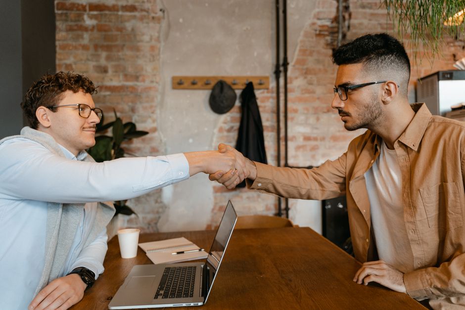 How to Negotiate Lower Interest Rates on Credit Cards: Debunking Common Myths Businessmen shaking hands over a laptop at a wooden table in a modern office setting.