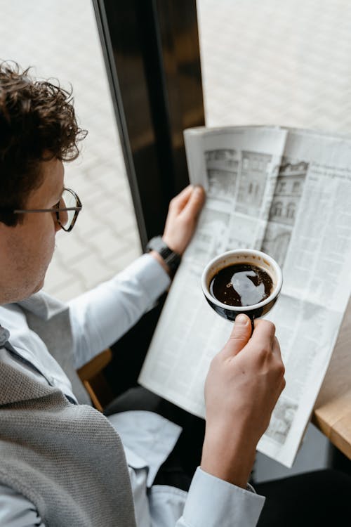 Free A Person with Eyeglasses  Holding a Cup of Coffee and a Newspaper Stock Photo