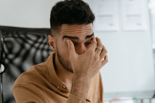 Close-up of a man rubbing his eyes, capturing stress or fatigue in an office environment.