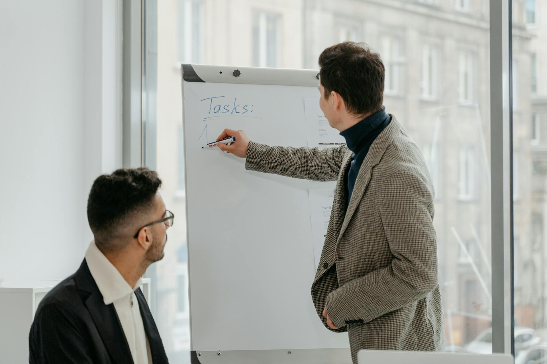 Man in Brown Suit Jacket Holding White Board