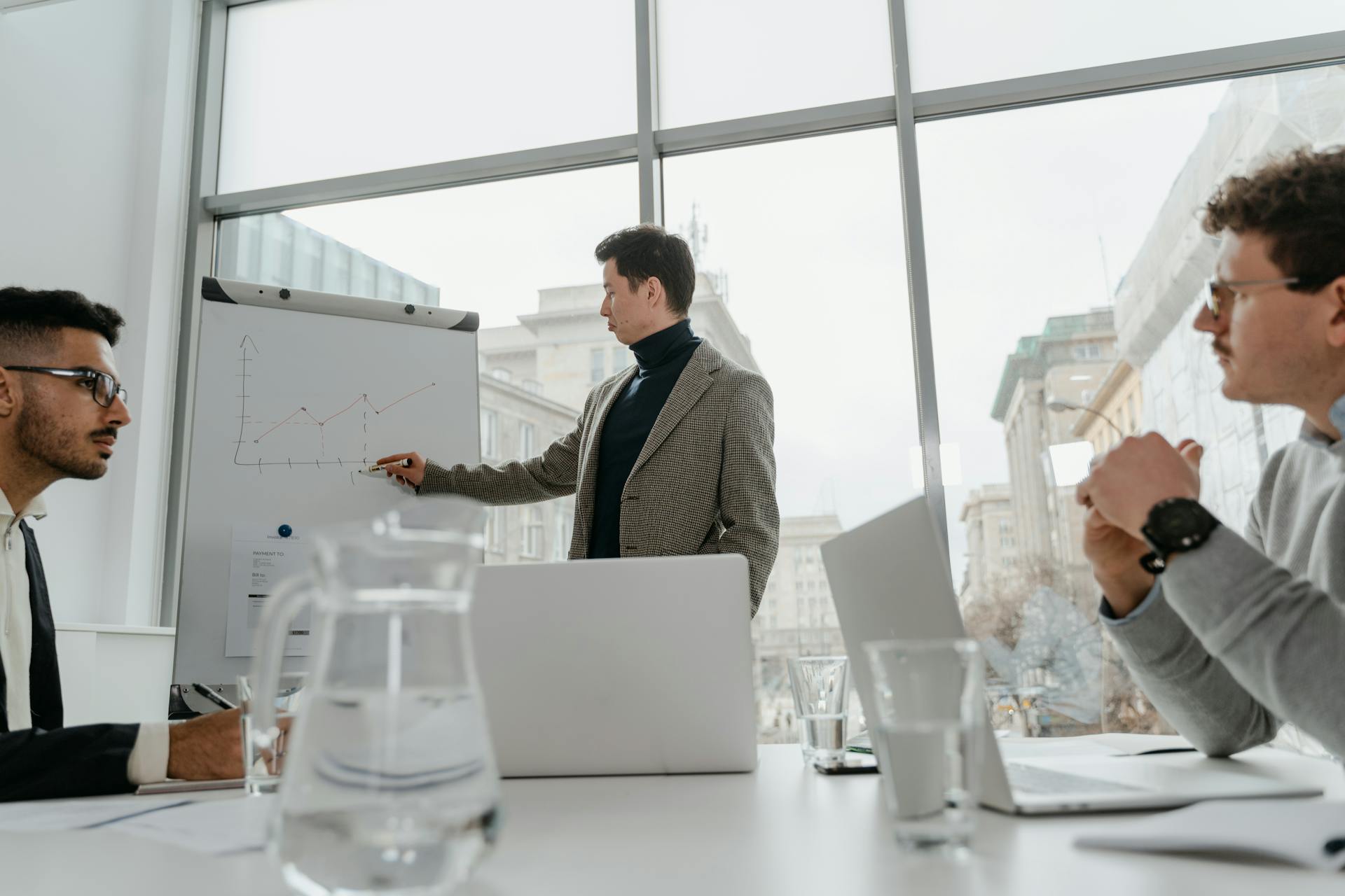 Professionals engaged in a collaborative business meeting with charts and laptops in a modern office setting.