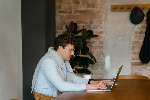 Man typing on laptop at a wooden desk in a cozy, rustic office space.