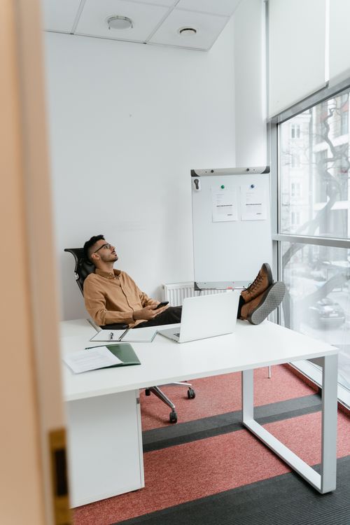 Free Man relaxing with feet up in a modern office setting, seated at a white desk. Stock Photo
