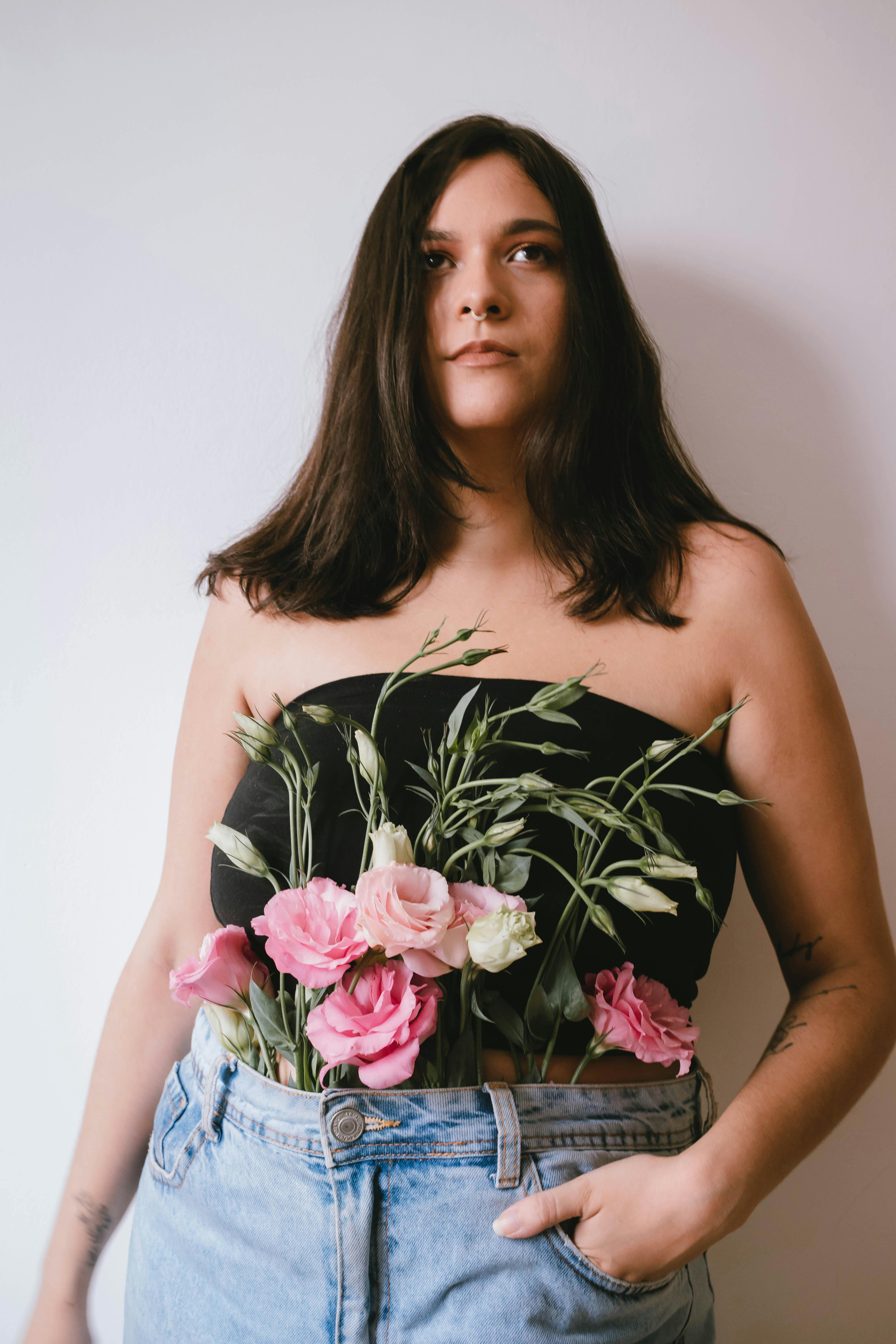 Artistic portrait of a woman with pink flowers creatively arranged in her outfit, set against a simple background.