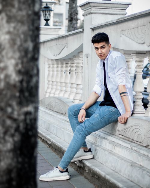 Free Young man in denim and white shirt sitting on a stone railing outdoors, Rasht, Iran. Stock Photo