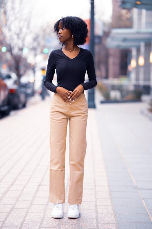 A Woman in Black Long Sleeves and Beige Pants Standing on the Street while Looking Over Shoulder