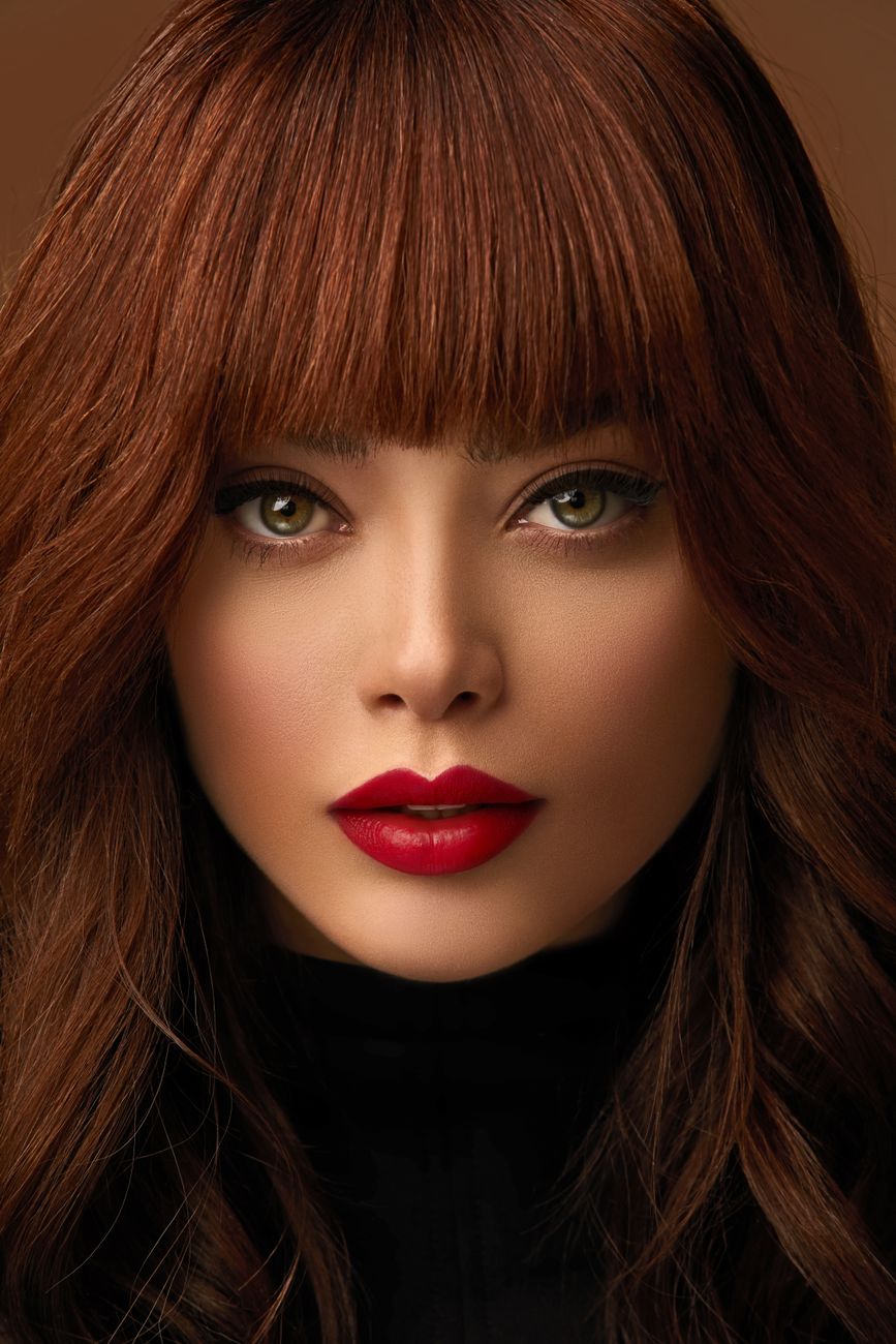 Close-up portrait of a woman with striking red lips and bangs, emphasizing beauty and style.