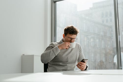 Free A Man Wearing Eyeglasses Holding a Smartphone While Drinking  Stock Photo