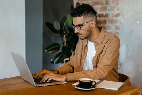 Free Young man with glasses working intently on laptop at a cafe. Stock Photo