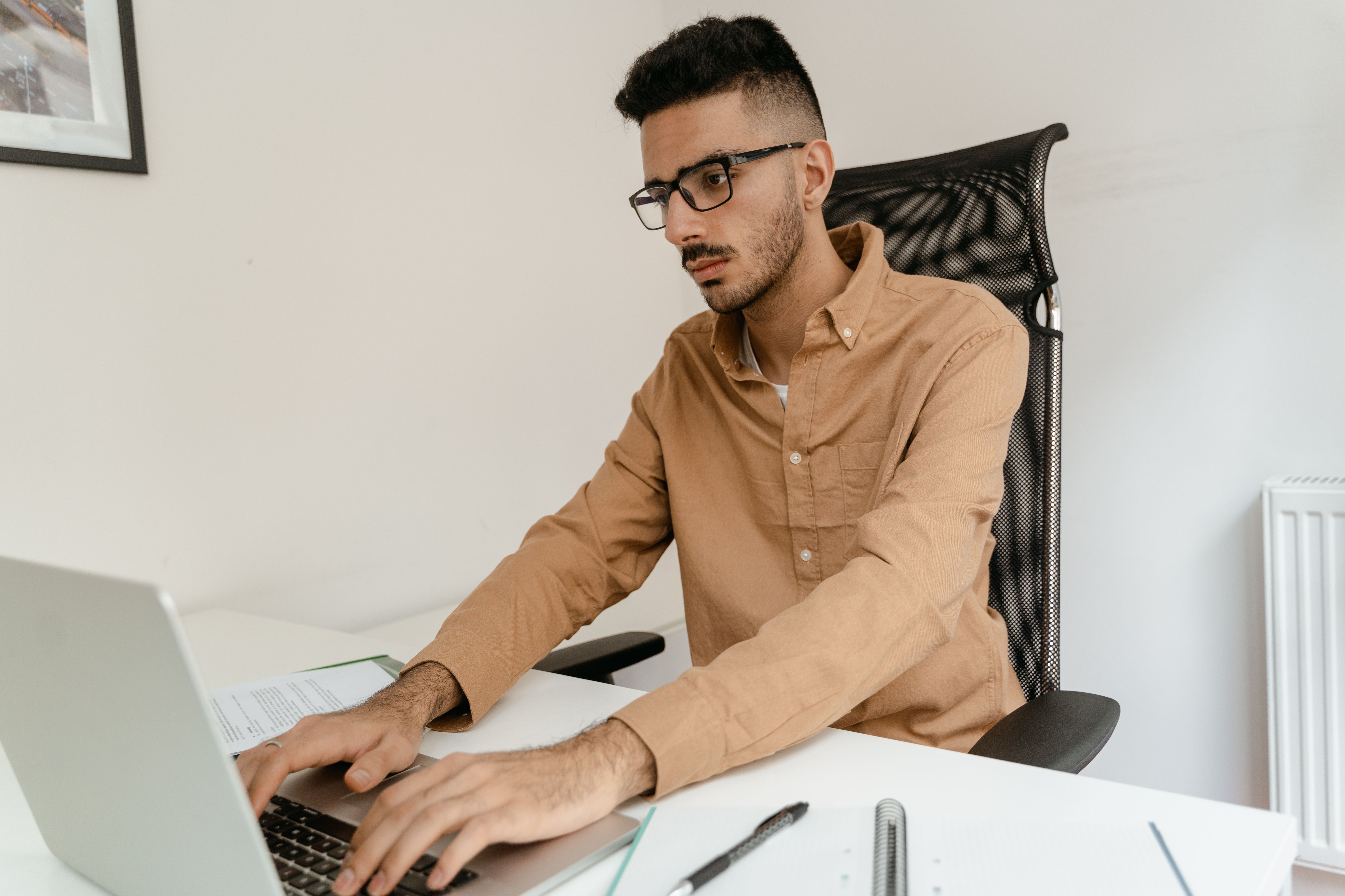 Man in brown shirt working on laptop, focused and indoors.
