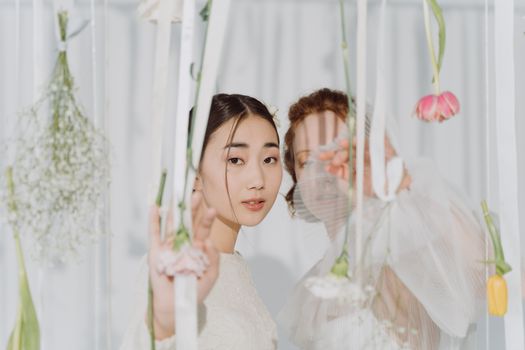 Two women posing elegantly among hanging flowers, showcasing delicate beauty and fashion.