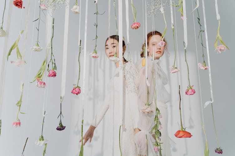 Women In White Dresses Behind Hanging Flowers