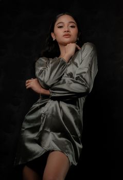 Beautiful portrait of an Asian woman posing elegantly in a satin dress against a dark background.