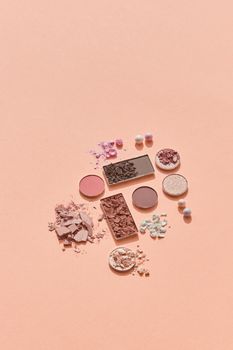 Artistic flat lay of crushed and pressed eyeshadows on a soft peach background, perfect for beauty blogs.