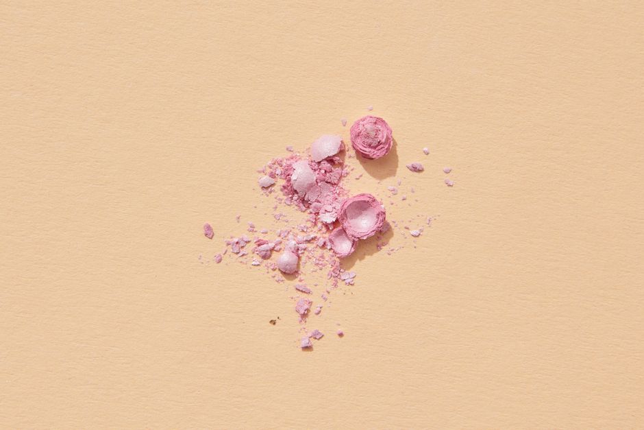Crushed pink makeup powder scattered on a light beige background, perfect for beauty and cosmetic themes.