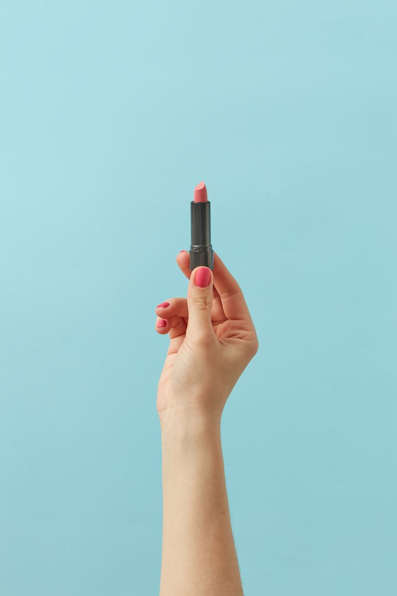 Hand holding a pink lipstick for application
