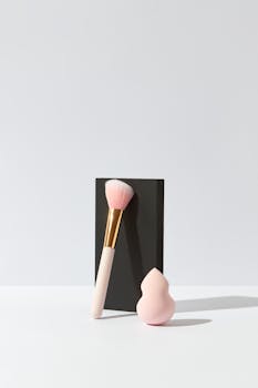 Elegant minimalist composition of a makeup brush and sponge blender on a white surface with a black background.