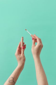 Hands holding a concealer applicator with a pastel blue background, showcasing beauty and cosmetics.