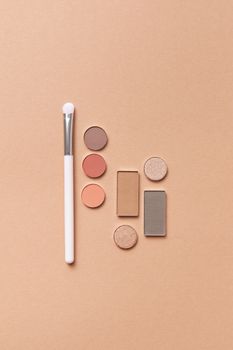 Flat lay of various makeup powders and a brush on a peach-toned background, ideal for beauty concepts.