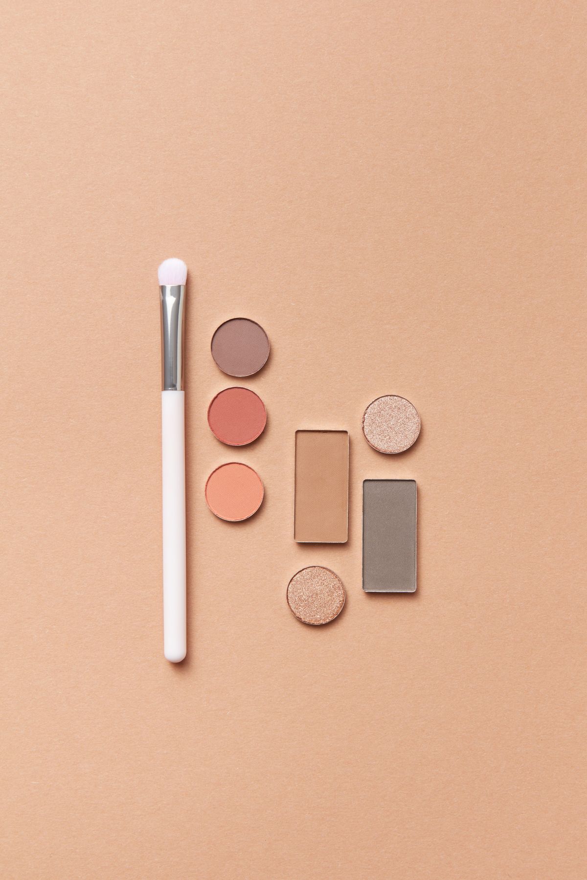 Makeup brush and eyeshadow palette flat lay on a peach background