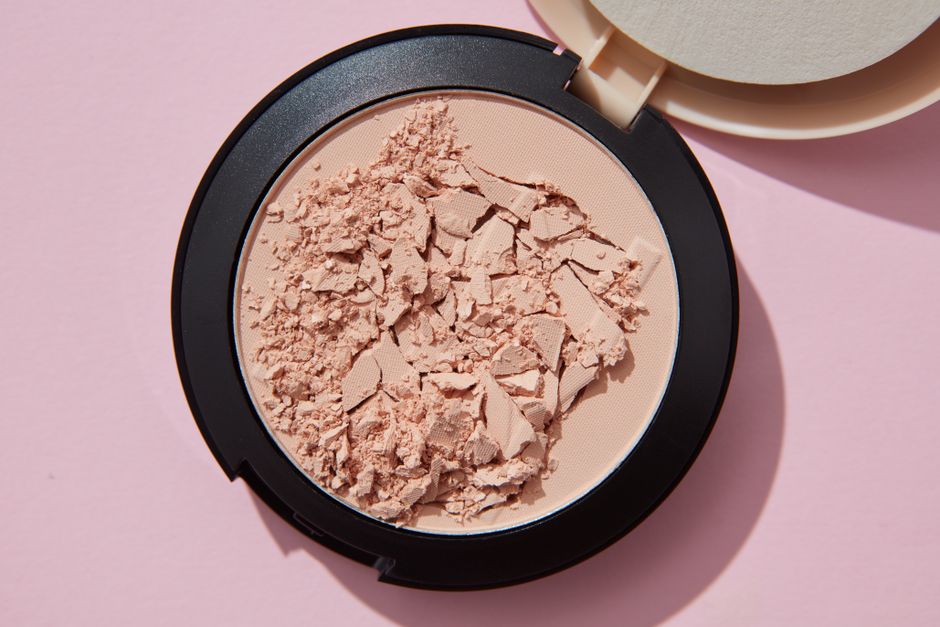 Close-up of crushed cosmetic powder in container against pink backdrop, showcasing texture and details.