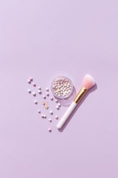 Flat lay of a makeup brush and pearlescent beads on a lavender background, highlighting beauty essentials.